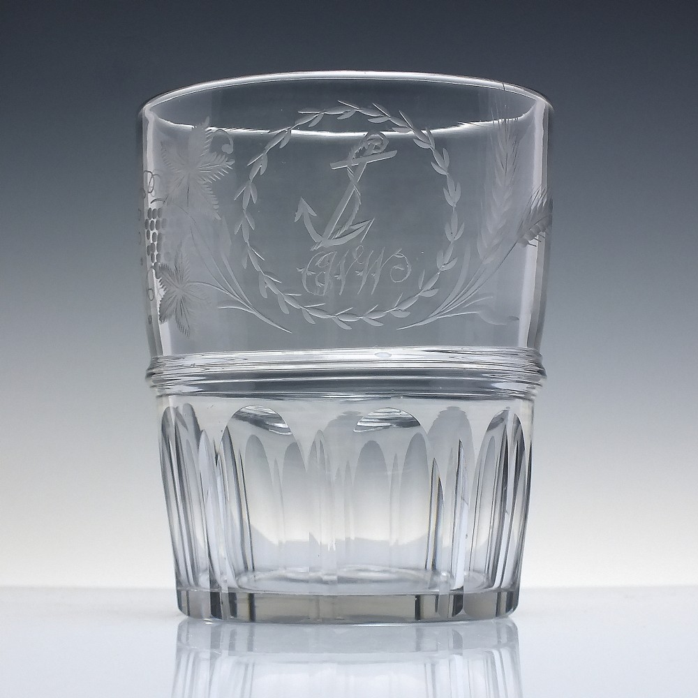 A clear Georgian lead crystal flip glass tumbler featuring lower cut panel flutes, a central waist ring, and upper wheel-engraved anchor and laurel wreath motifs.