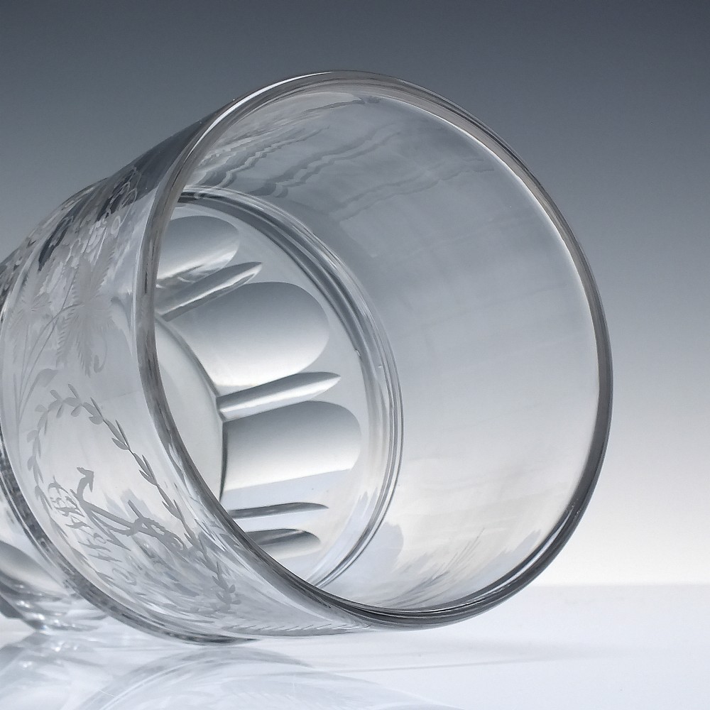 A clear Georgian lead crystal flip glass tumbler featuring lower cut panel flutes, a central waist ring, and upper wheel-engraved anchor and laurel wreath motifs. View V