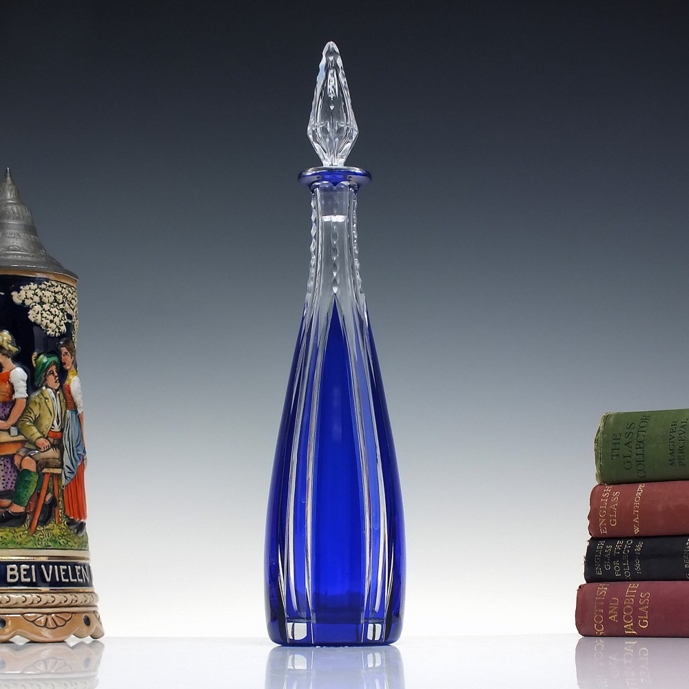 A tall, slender cobalt blue cut-to-clear crystal spirit decanter featuring vertical faceted flutes and a pointed, clear faceted stopper.