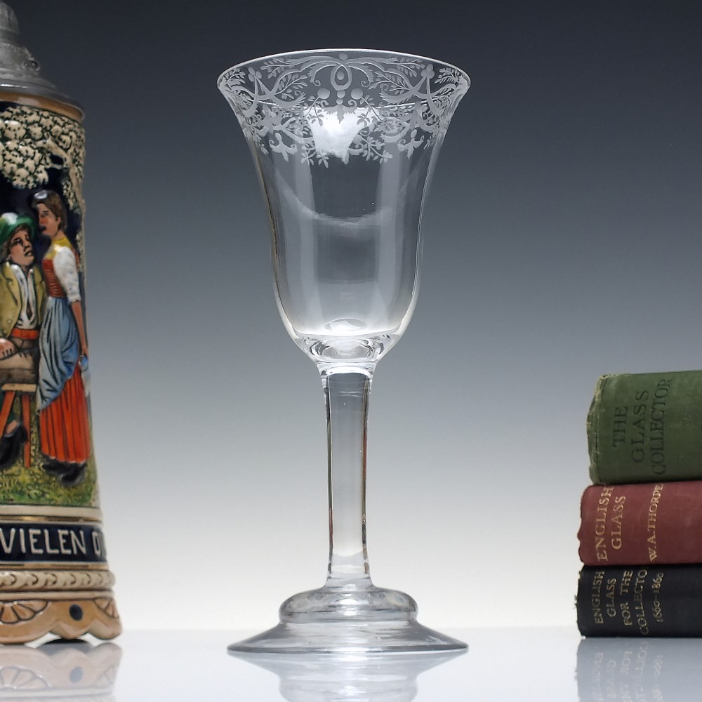 A clear 18th-century lead glass goblet featuring an engraved scroll border along the rim, a plain stem, and a circular foot.