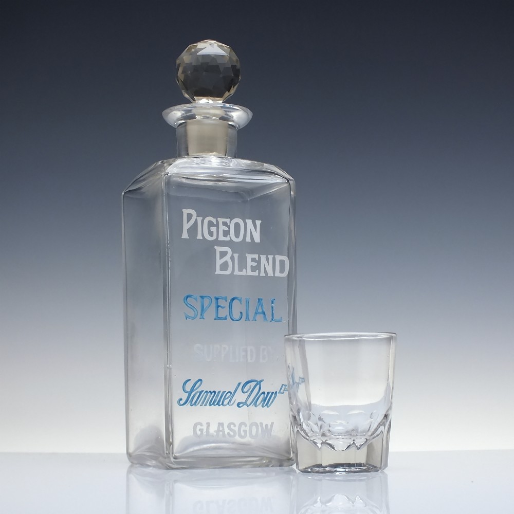 A rectangular clear glass whisky decanter featuring white and blue enamelled text reading Pigeon Blend Special and topped with a faceted glass stopper. View III