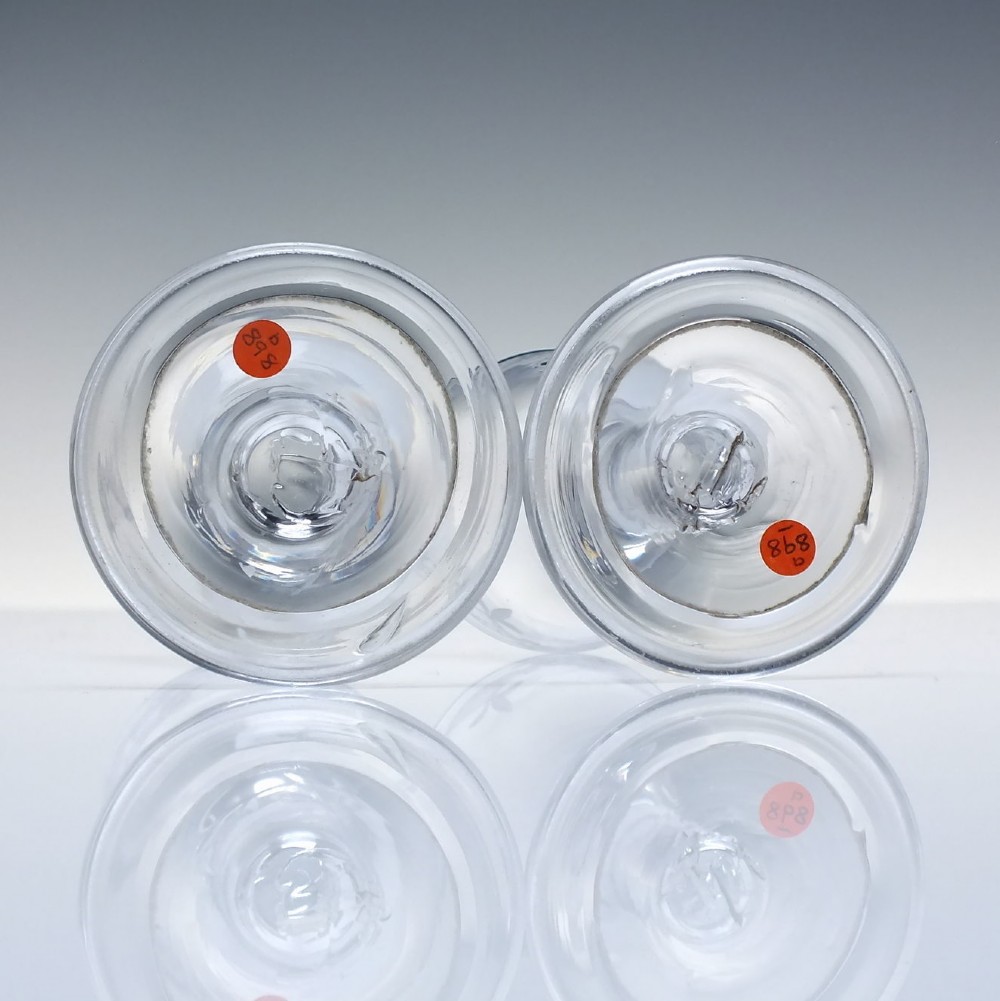 A pair of 18th-century clear glass drams featuring wheel-engraved draped swag borders, plain stems, and wide folded feet. View V