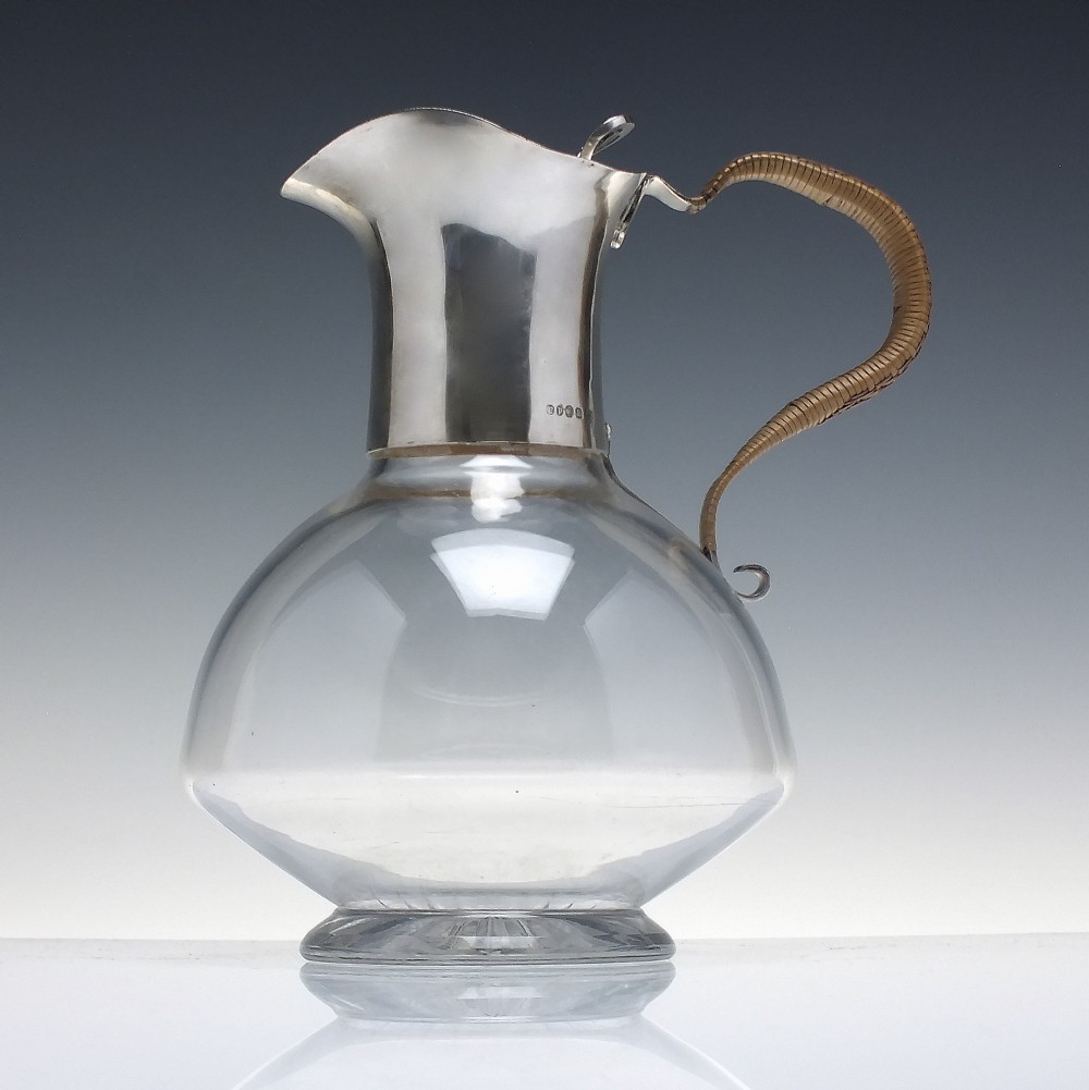 A late Victorian clear glass claret jug featuring a silver-plated neck, hinged lid, spout, and a cane-wrapped curved handle.