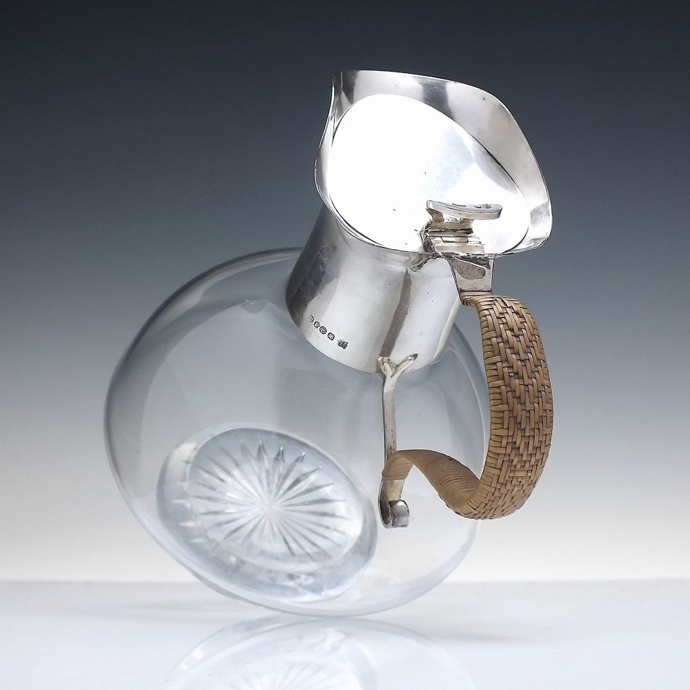A late Victorian clear glass claret jug featuring a silver-plated neck, hinged lid, spout, and a cane-wrapped curved handle. View VI