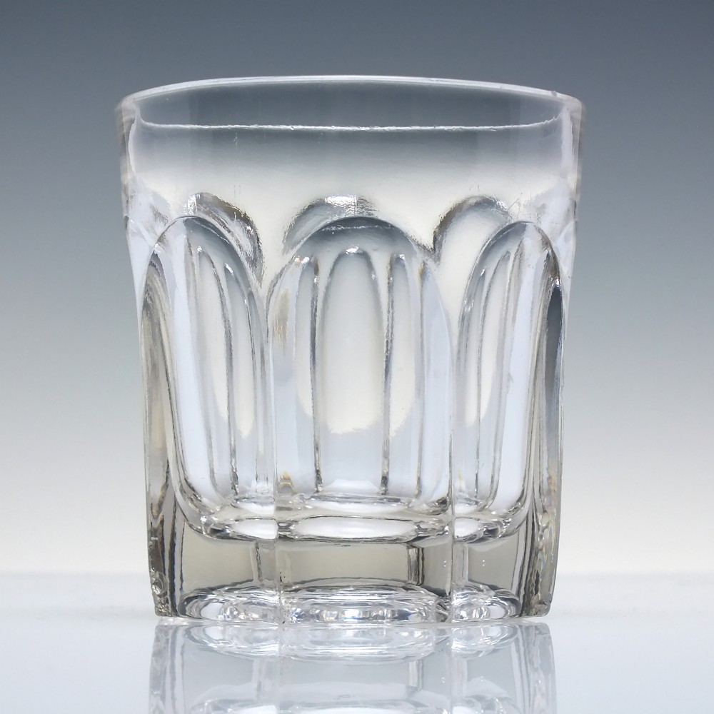 A clear Victorian glass whisky tumbler featuring fluted arch cuttings around the lower body and a thick base.