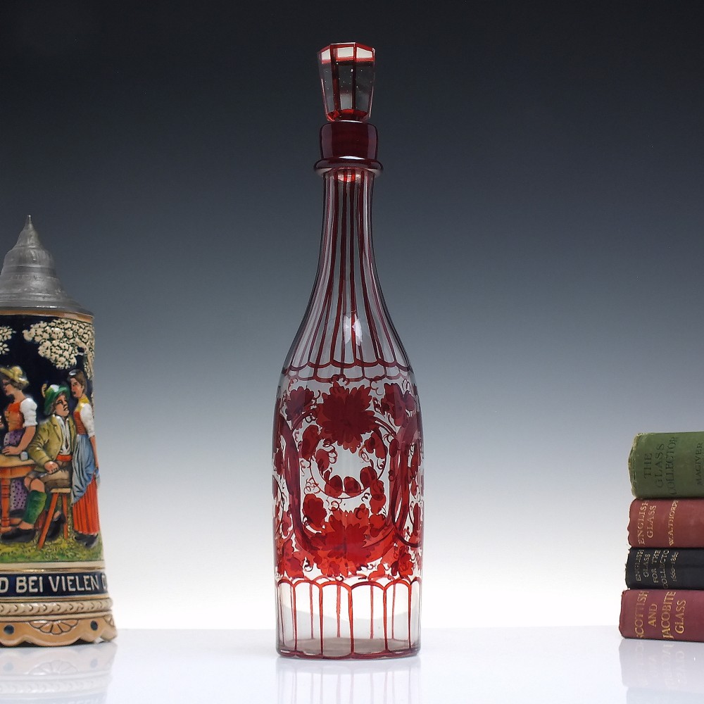 A tall clear glass decanter featuring red hand-painted floral motifs, vertical stripes, and a faceted glass stopper.