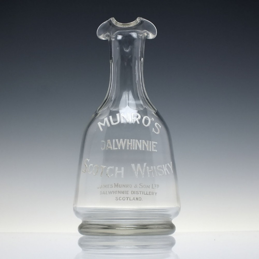 A clear glass antique whisky water carafe featuring white enamelled lettering for Dalwhinnie Scotch Whisky and a pinched pour spout.