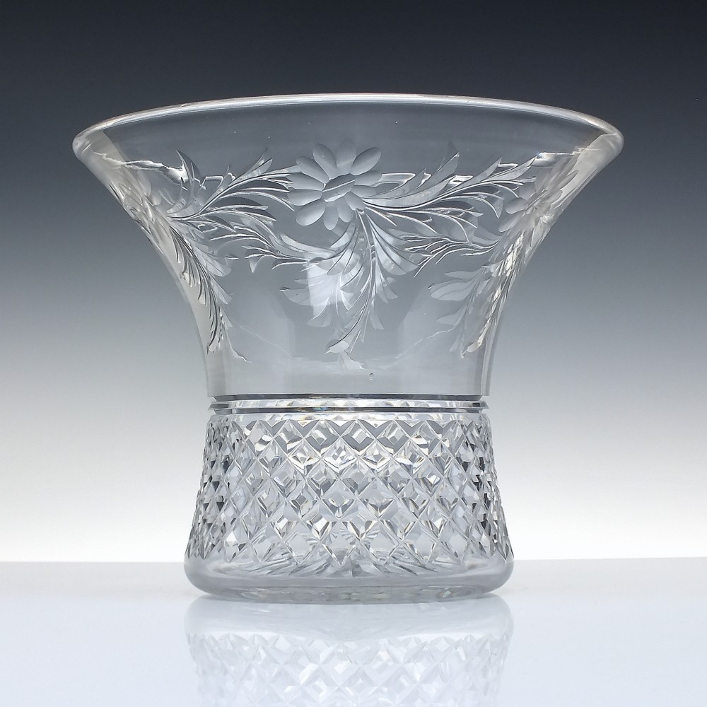 A clear cut crystal vase featuring a flared upper rim with engraved floral details above a geometric diamond-cut lower body.