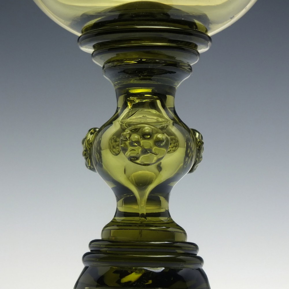 An olive green glass roemer goblet featuring a bulbous bowl, a central stem adorned with applied prunts, and a flared ribbed pedestal base. View V