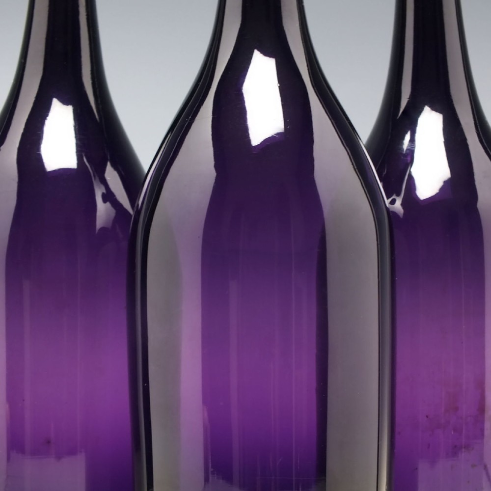 A set of three Victorian hand-blown deep purple amethyst glass wine serving bottles featuring long tapered necks and double ring lip collars. View IV