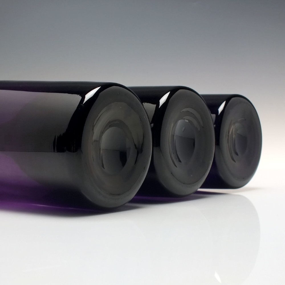 A set of three Victorian hand-blown deep purple amethyst glass wine serving bottles featuring long tapered necks and double ring lip collars. View V