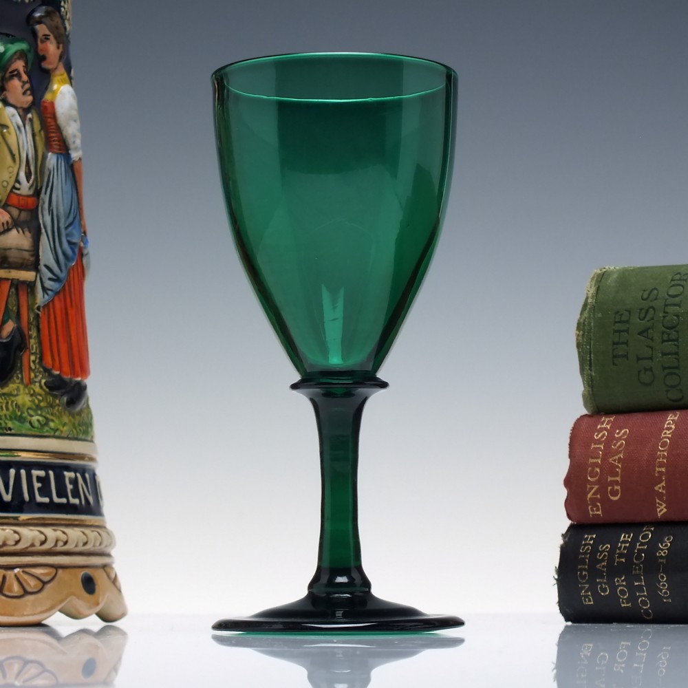 A mid-nineteenth-century wine glass made from deep emerald green glass with a slender stem and flat circular foot.