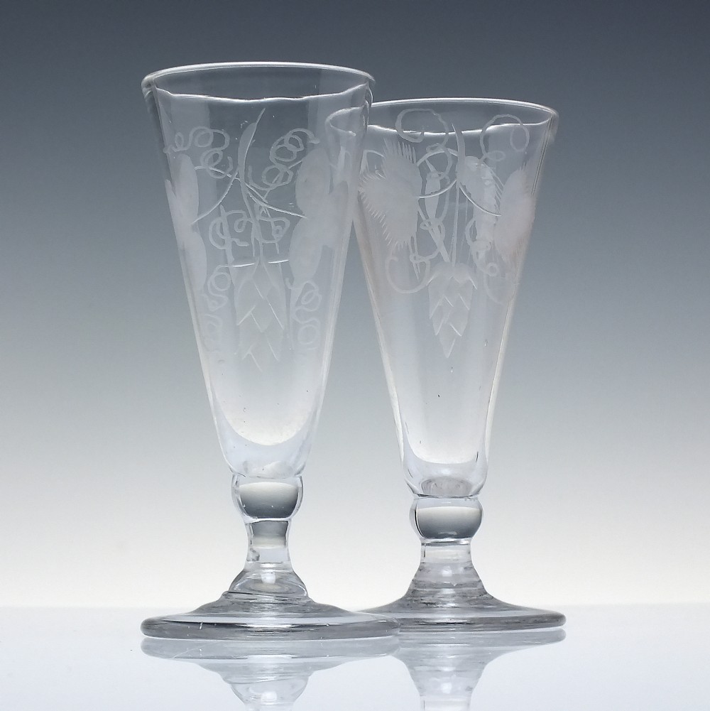 Pair of clear Georgian lead glass ale flutes featuring wheel-engraved barley and hops decoration on knopped stems.