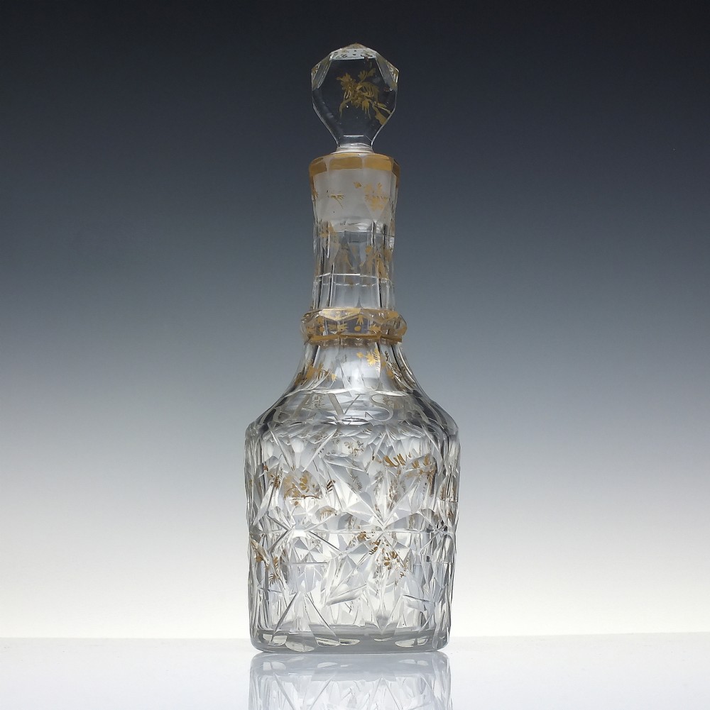 A clear cut glass decanter with gilded lettering on the shoulder, a diamond facetted body, and a facetted glass stopper. View II