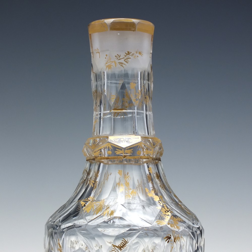 A clear cut glass decanter with gilded lettering on the shoulder, a diamond facetted body, and a facetted glass stopper. View III