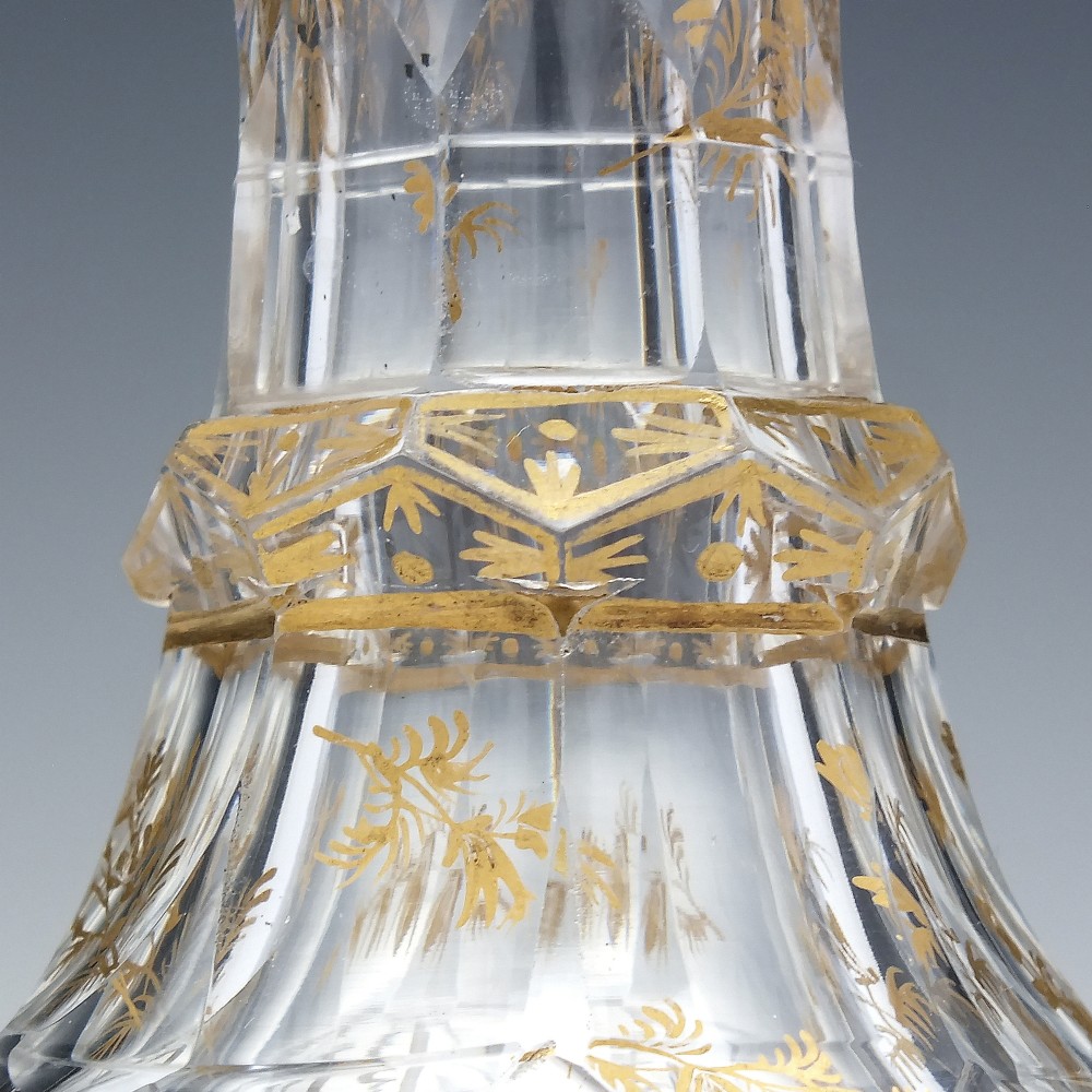 A clear cut glass decanter with gilded lettering on the shoulder, a diamond facetted body, and a facetted glass stopper. View V