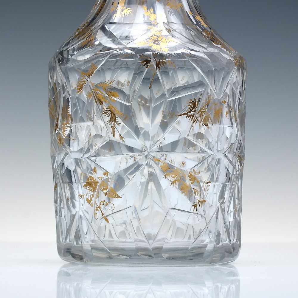A clear cut glass decanter with gilded lettering on the shoulder, a diamond facetted body, and a facetted glass stopper. View VII