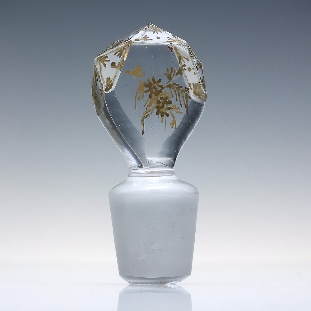 A clear cut glass decanter with gilded lettering on the shoulder, a diamond facetted body, and a facetted glass stopper. View XII