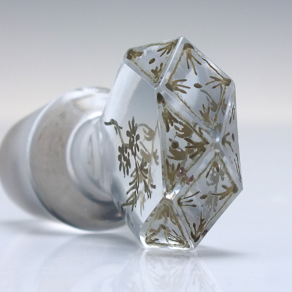 A clear cut glass decanter with gilded lettering on the shoulder, a diamond facetted body, and a facetted glass stopper. View XIII