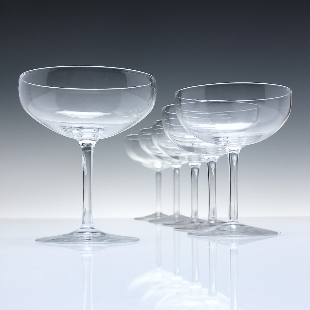 A set of six clear Edwardian crystal champagne coupes with wide saucer bowls and slender stems arranged in a line.