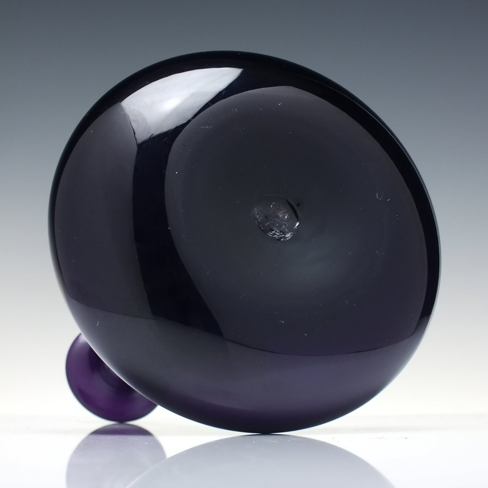A deep purple amethyst glass decanter featuring a wide bulbous base, elongated neck, and a metal ring stopper engraved with the word BRANDY. View VI