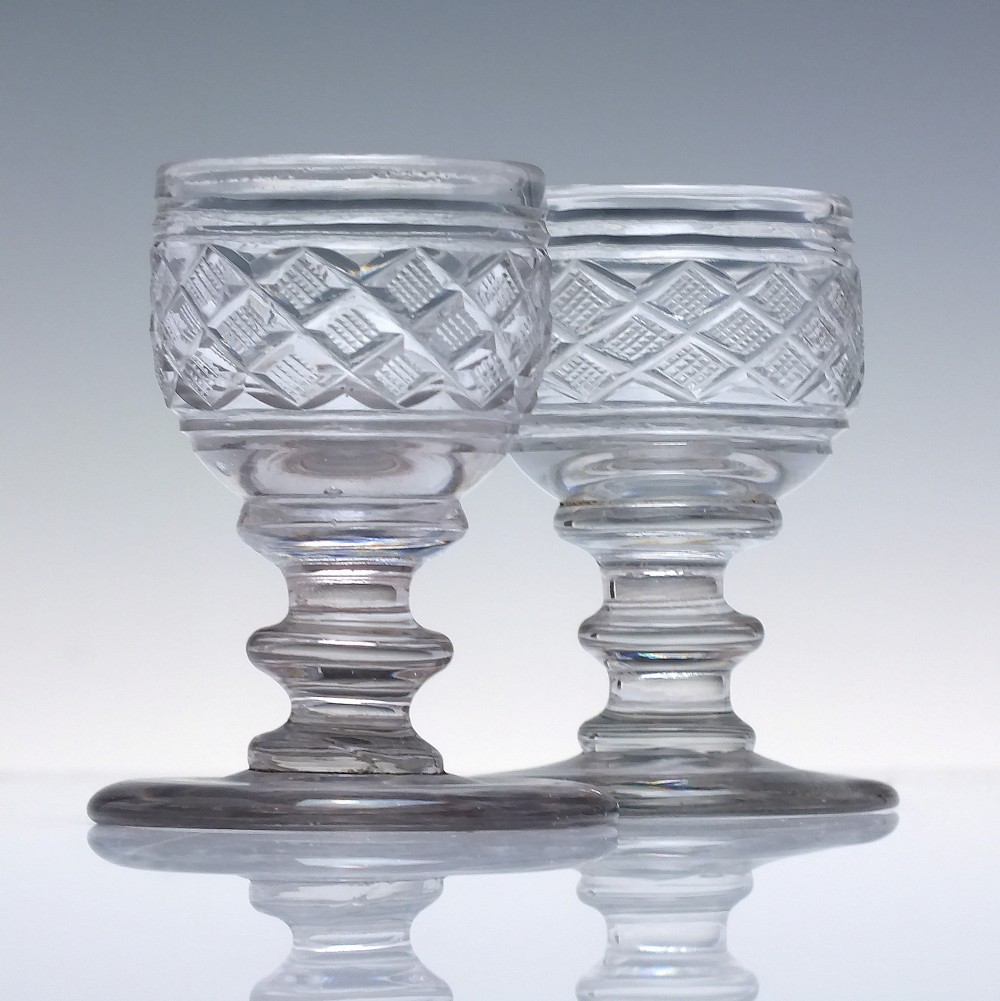 A pair of early 19th-century clear cut lead crystal dram glasses featuring diamond cutting and knopped stems.