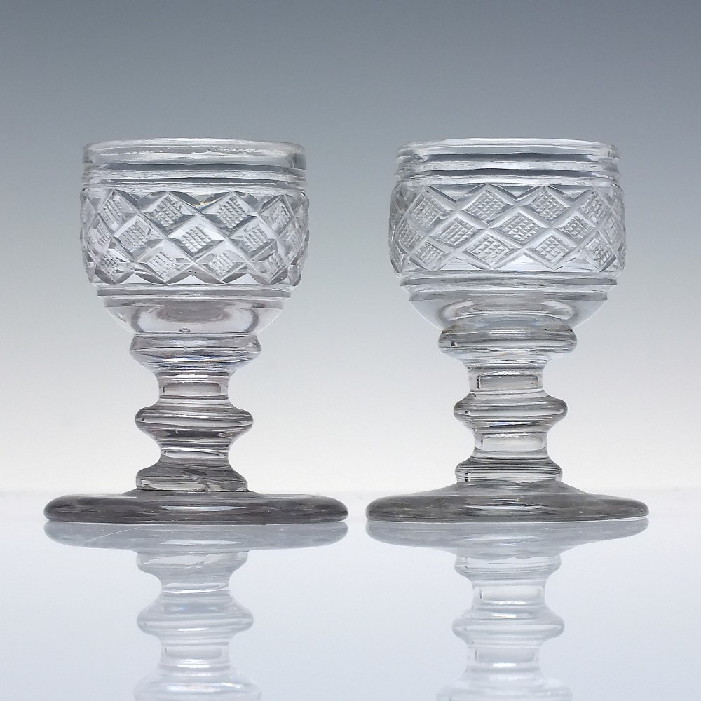 A pair of early 19th-century clear cut lead crystal dram glasses featuring diamond cutting and knopped stems. View II