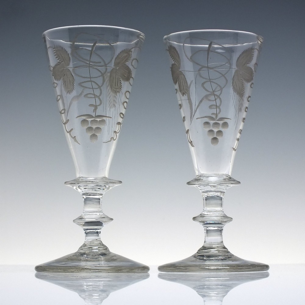 A pair of clear hand-blown Georgian glass goblets featuring wheel-engraved motifs of hops and barley on conical bowls above knopped stems and conical bases.