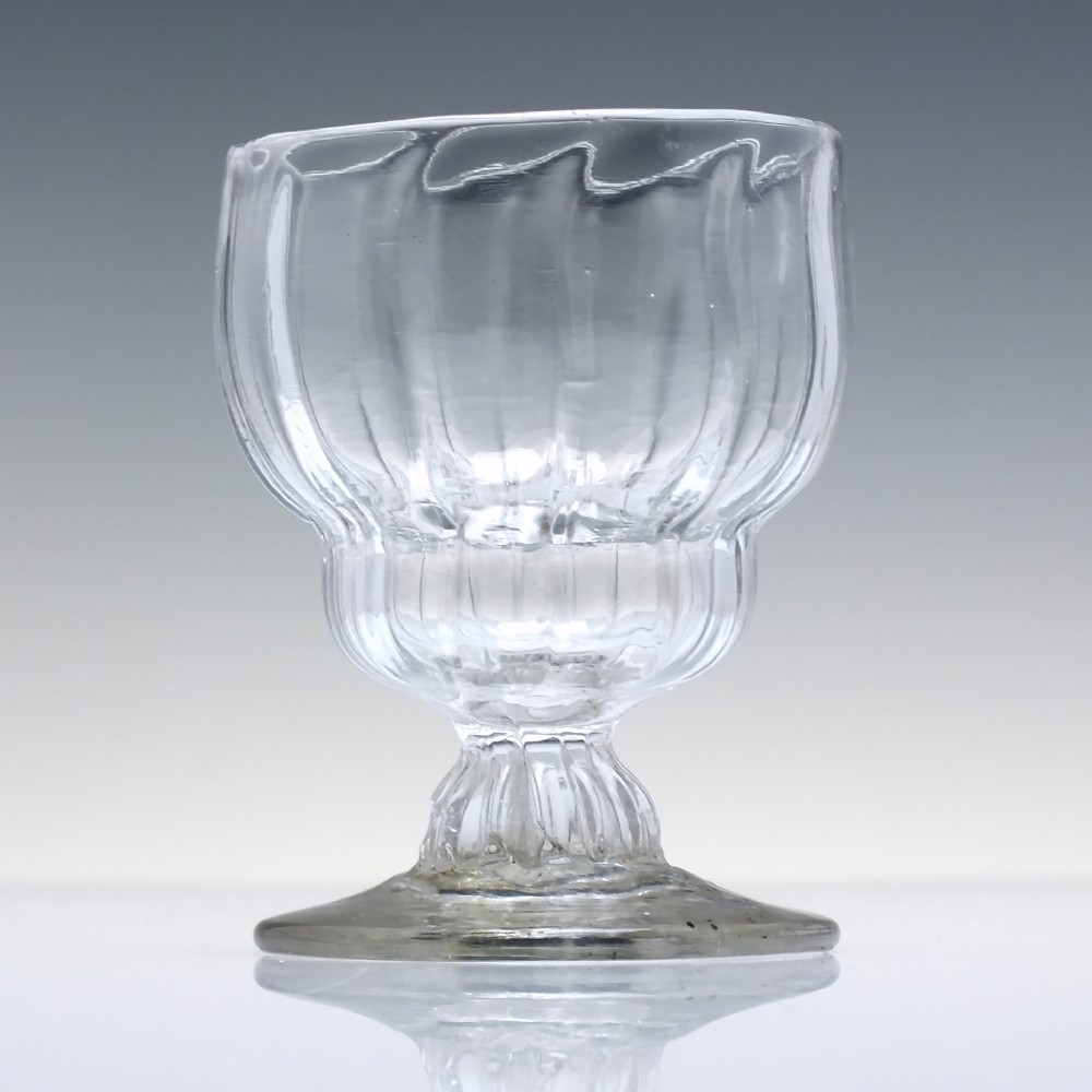 A small Georgian clear lead glass bonnet glass featuring a rib-moulded double-curved bowl, short pedestal stem, and flat circular foot. View II