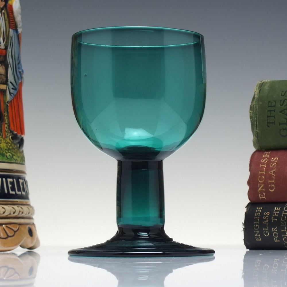 An 18th-century emerald green hand-blown glass wine goblet featuring a rounded cup, thick cylindrical stem, and circular foot.