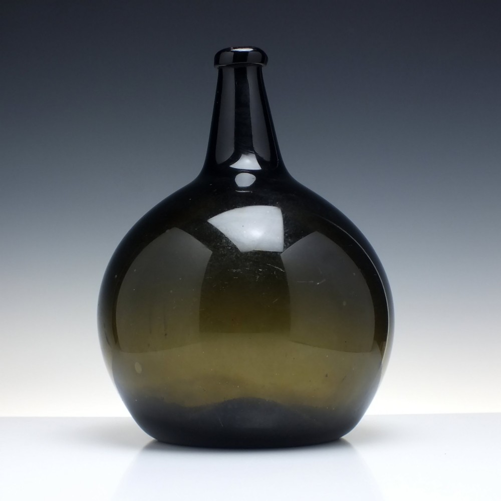 A large, dark green hand-blown antique glass wine bottle with a bulbous body and tapered neck.