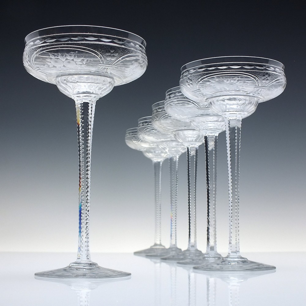 A set of six French Art Nouveau clear lead crystal champagne coupes with tall beaded stems and etched floral motifs on shallow bowls.