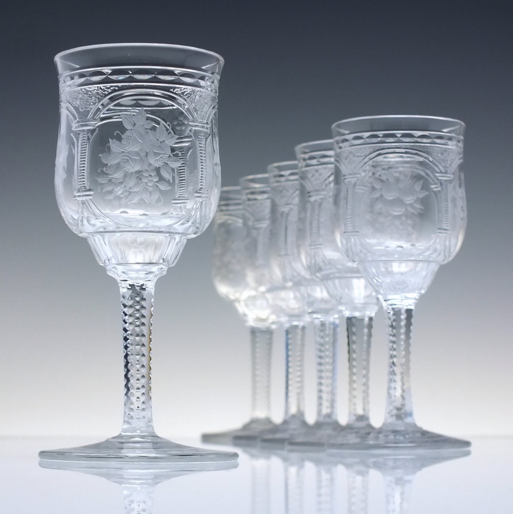 A set of six clear lead crystal dram glasses featuring acid-etched floral panels set within archways and faceted diamond-cut stems.