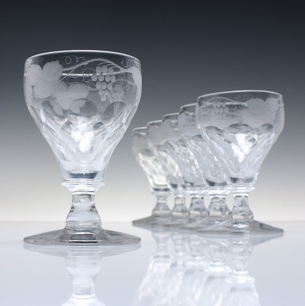 A set of six vintage clear glass port goblets featuring wheel-engraved grapevine motifs on pan-topped bowls with cut facet details.