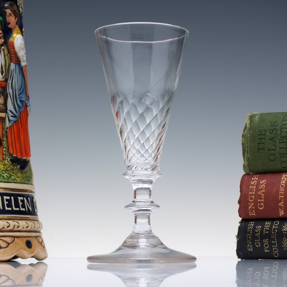 A clear Georgian ale glass featuring half-wrythen spiral moulding on the conical bowl above a knopped stem.