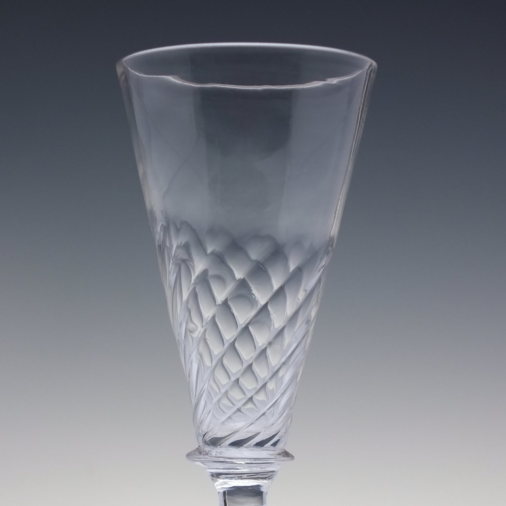 A clear Georgian ale glass featuring half-wrythen spiral moulding on the conical bowl above a knopped stem. View II