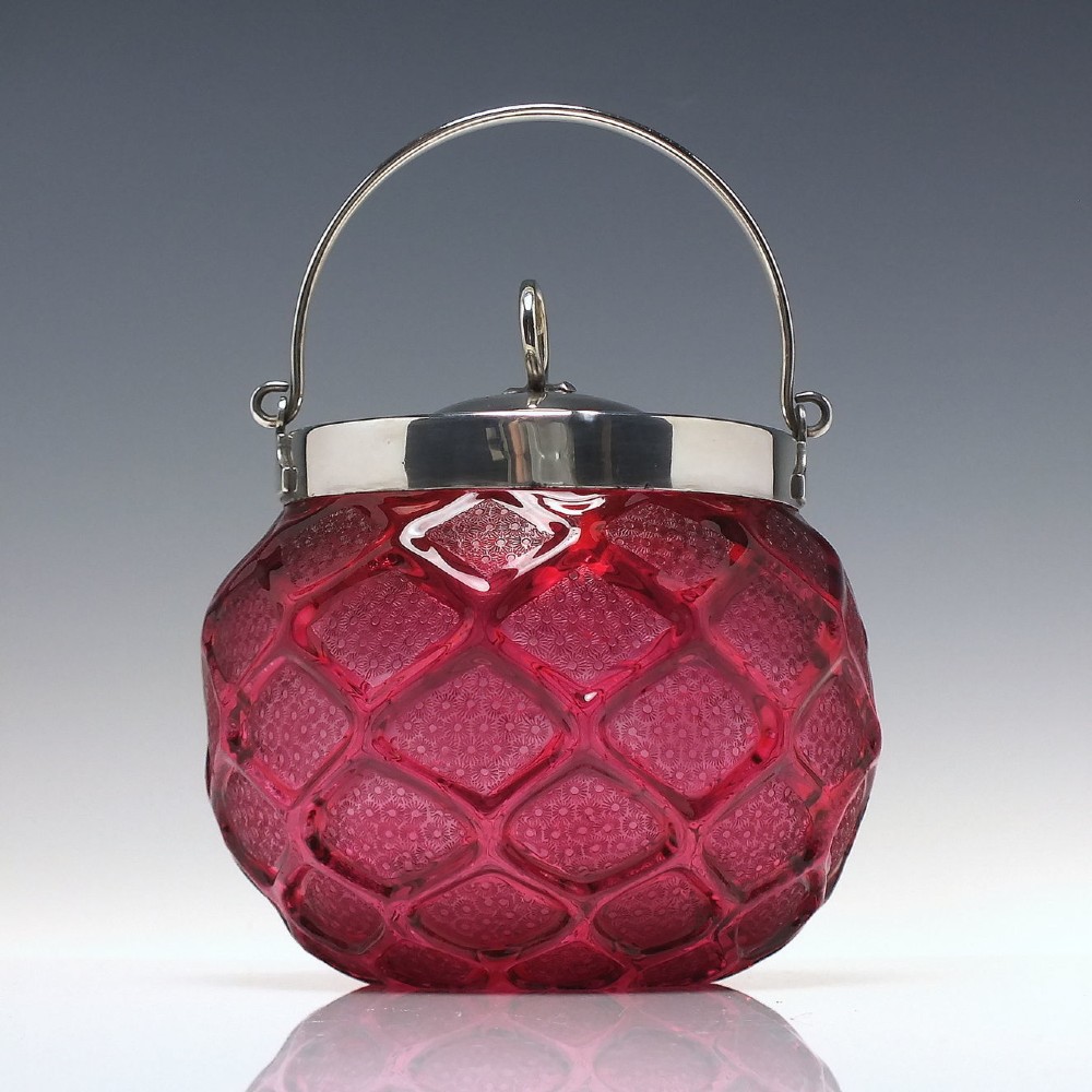 A Victorian cranberry glass biscuit barrel featuring a diamond-quilted pattern with internal floral etching and a silver-plated rim, lid, and overhead swing handle.