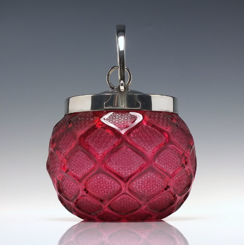 A Victorian cranberry glass biscuit barrel featuring a diamond-quilted pattern with internal floral etching and a silver-plated rim, lid, and overhead swing handle. View II