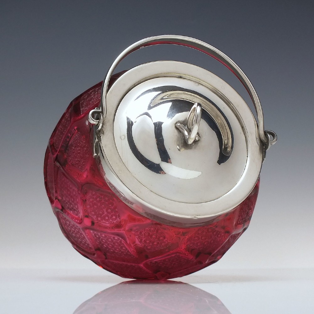 A Victorian cranberry glass biscuit barrel featuring a diamond-quilted pattern with internal floral etching and a silver-plated rim, lid, and overhead swing handle. View III