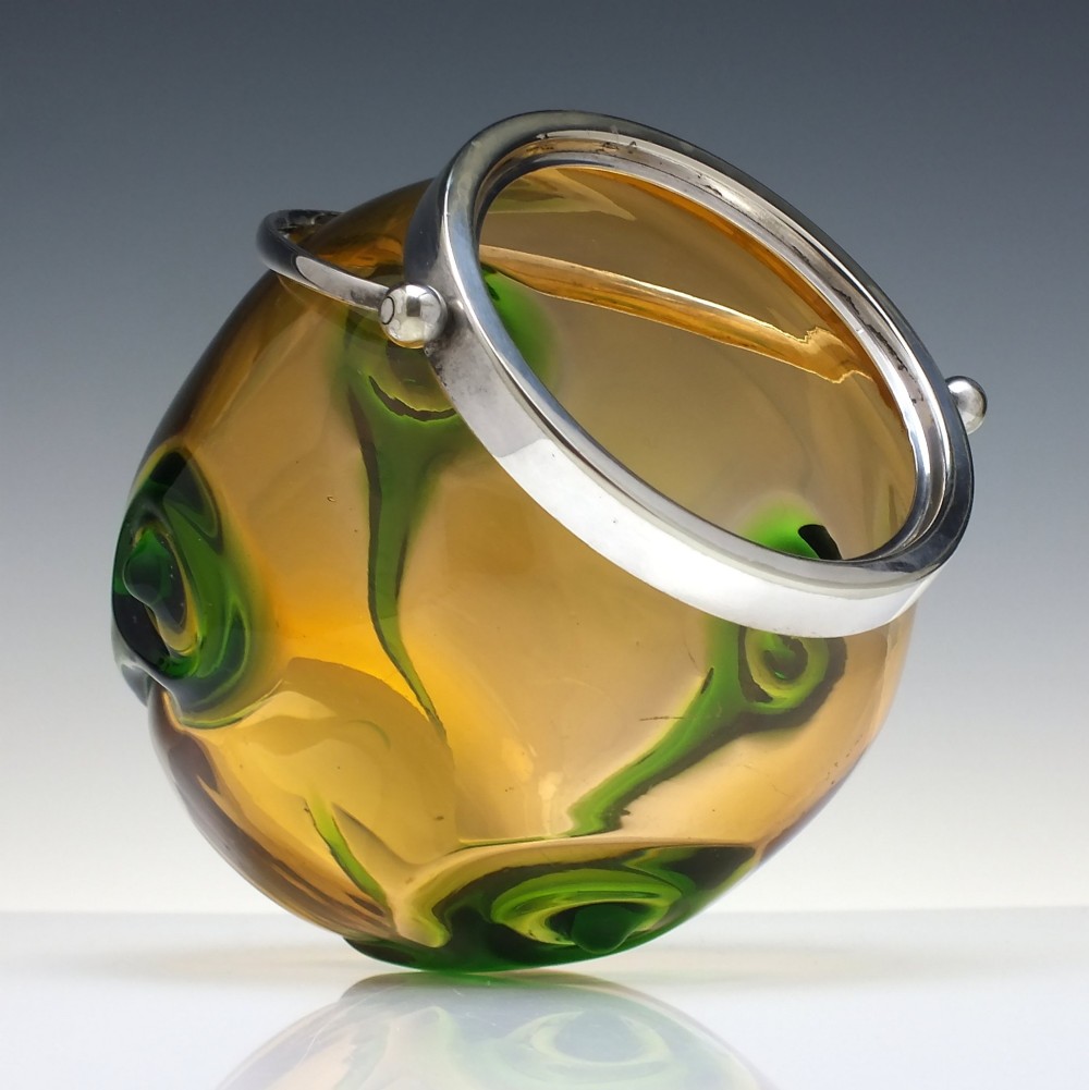 An Art Nouveau amber glass biscuit barrel featuring green peacock eye trailing decoration and a silver-plated metal rim, lid, and swing handle. View IV