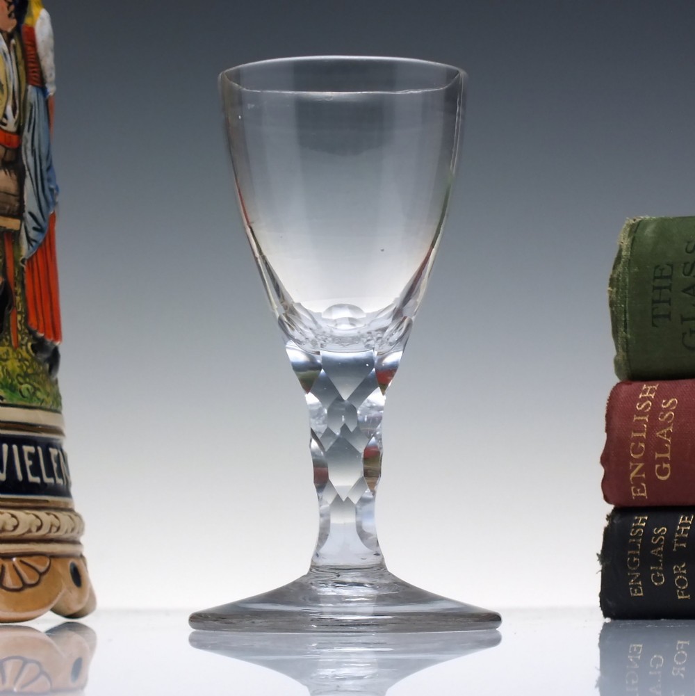 An 18th-century clear lead crystal dram glass with a rounded bowl and a diamond facet-cut stem resting on a circular base.