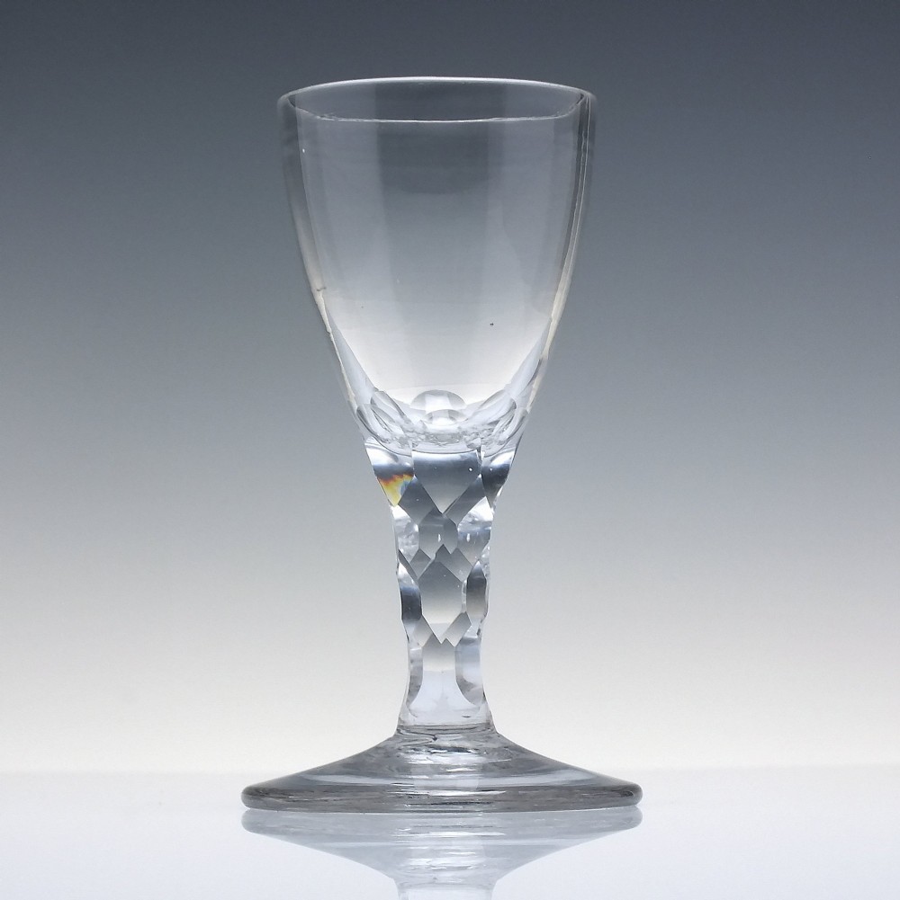 An 18th-century clear lead crystal dram glass with a rounded bowl and a diamond facet-cut stem resting on a circular base. View II