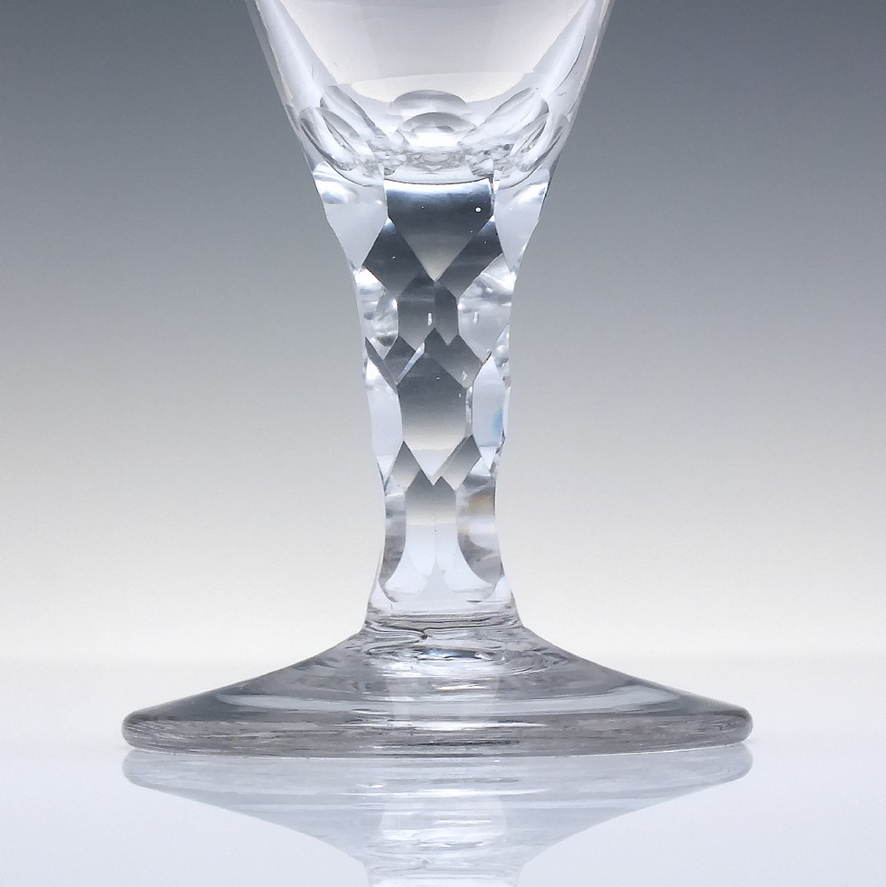 An 18th-century clear lead crystal dram glass with a rounded bowl and a diamond facet-cut stem resting on a circular base. View III
