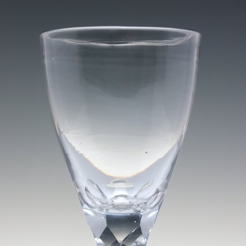 An 18th-century clear lead crystal dram glass with a rounded bowl and a diamond facet-cut stem resting on a circular base. View IV
