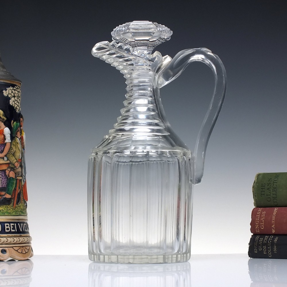 A clear Georgian Regency cut glass claret jug with a step-cut neck, panelled body, applied handle, and faceted stopper.