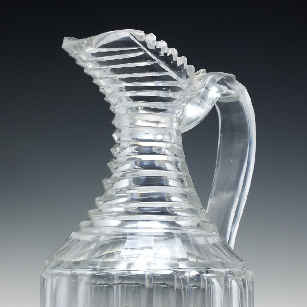 A clear Georgian Regency cut glass claret jug with a step-cut neck, panelled body, applied handle, and faceted stopper. View IV