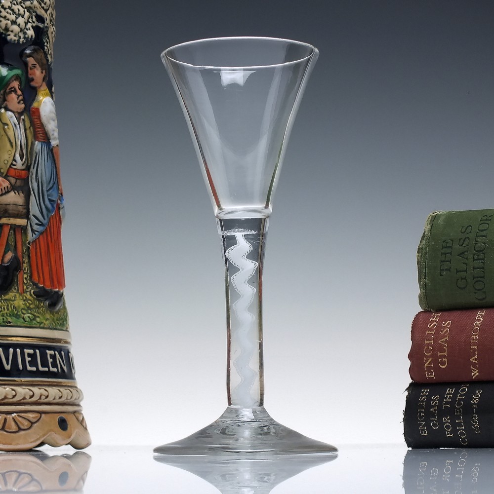 An 18th-century clear lead glass wine glass featuring a flared trumpet bowl, a central white opaque twist stem, and a circular conical foot.