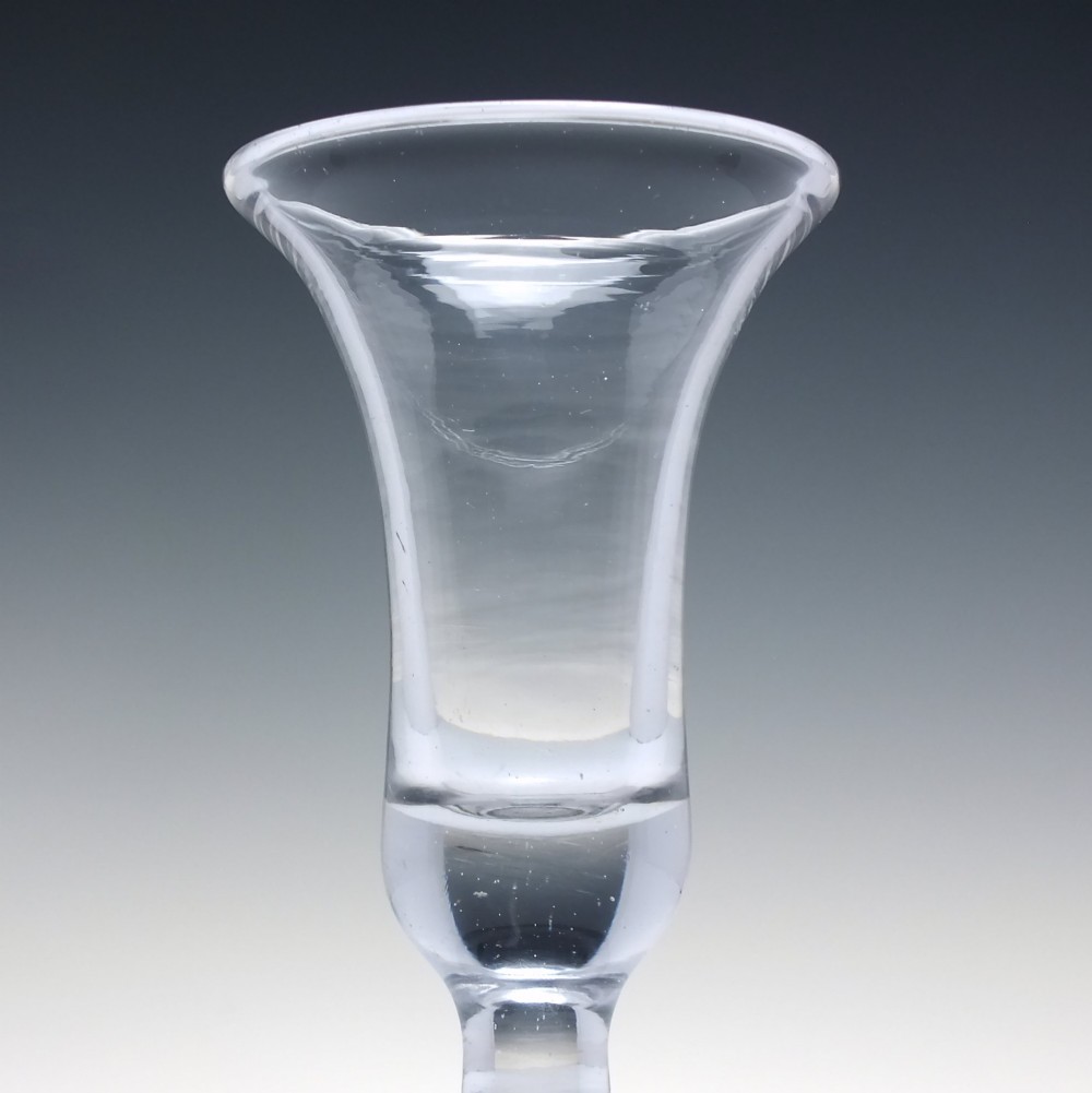 An 18th-century clear glass firing glass featuring a flared trumpet rim, short stem element, and a heavy, thick round foot. View III
