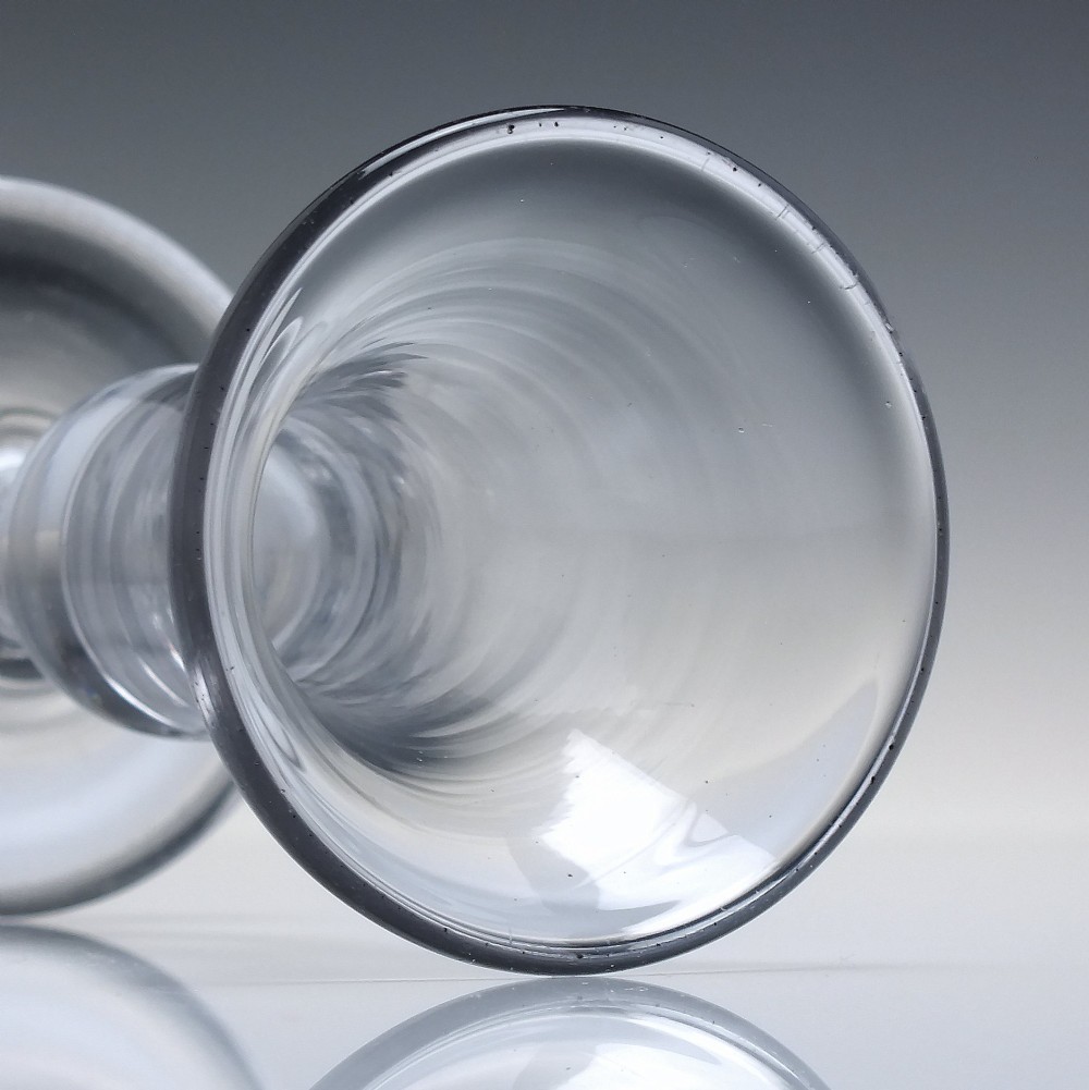 An 18th-century clear glass firing glass featuring a flared trumpet rim, short stem element, and a heavy, thick round foot. View IV