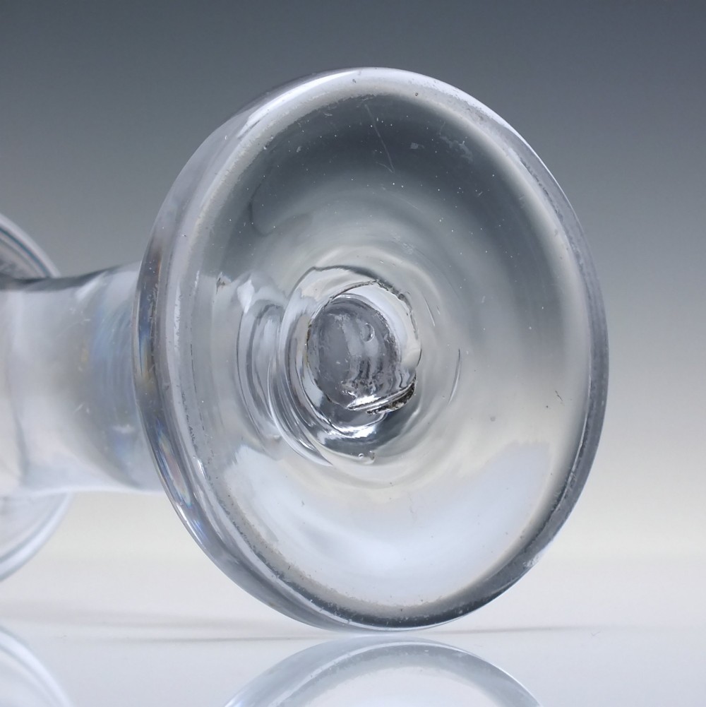 An 18th-century clear glass firing glass featuring a flared trumpet rim, short stem element, and a heavy, thick round foot. View V